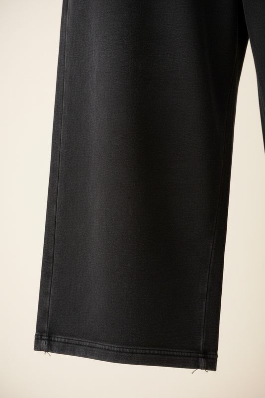 podea. heavyweight joggers flat lay in washed black on linen surface, wide leg silhouette and straight open hem visible, diagonal light, no figure