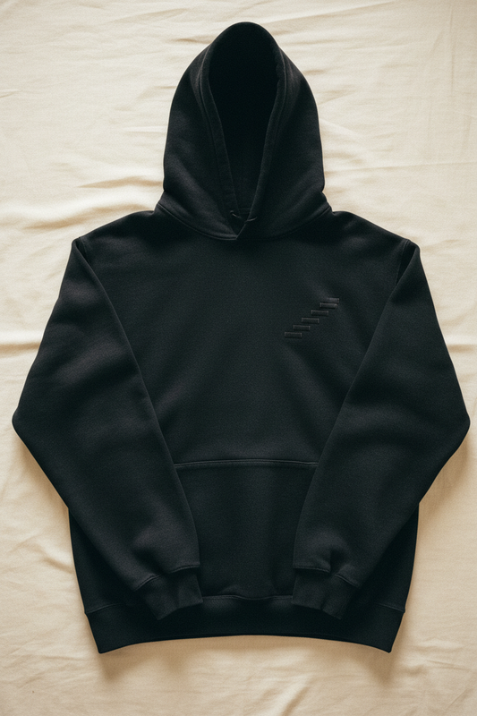 echelonn. aegis. heavyweight hoodie laid flat on concrete floor under skylight — 400gsm loop-back fleece, washed black