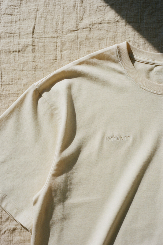 echelonn. peplos. oversized tee in stone — shoulder seam and dropped sleeve detail, tonal wordmark, natural light on linen