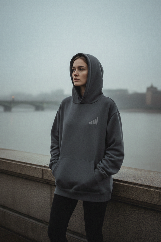light-skinned female figure wearing grey aegis. heavyweight hoodie on Thames embankment at dawn, grey river and grey sky behind, morning mist, cinematic editorial