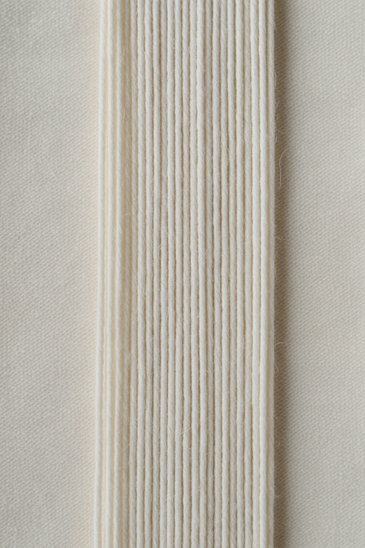 Combed cotton yarn macro showing smooth aligned parallel fibres with no protruding ends, fine ring-spun thread on off-white surface