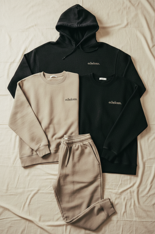 echelonn. aegis. hoodie and thorax. sweatshirt hanging in brutalist concrete room — washed black and stone, tonal echelonn. wordmark on left chest
